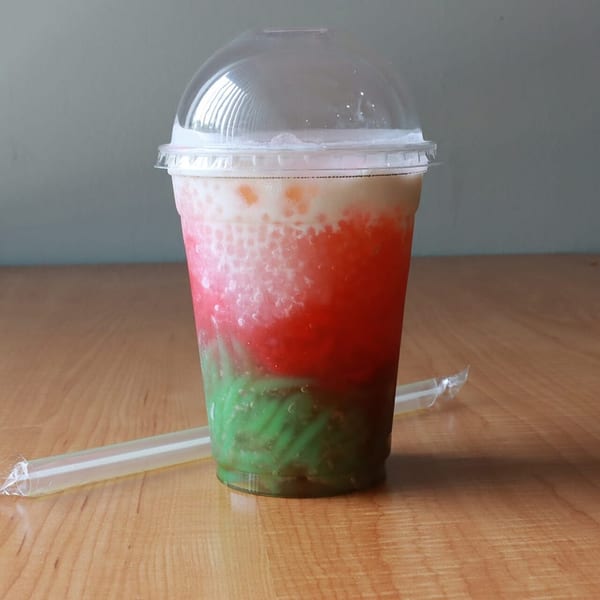 Colorful Thai dessert drink with layers of white, red, and green ingredients in a clear cup.