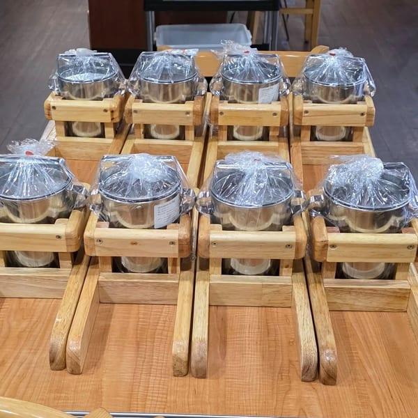 Eight Thai hot pots with metal inserts and wooden frames, wrapped in plastic, on a wooden table.