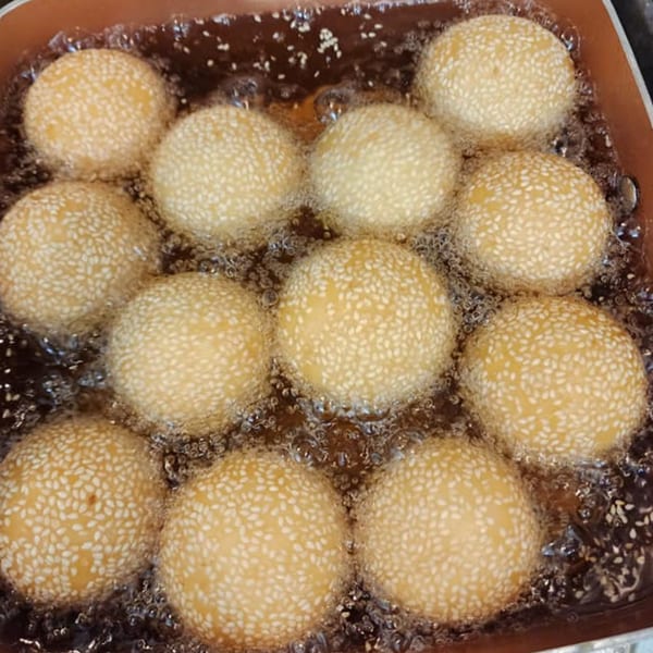 Sesame balls, a Thai dessert, deep-frying in hot oil, bubbling around the golden-brown spheres.