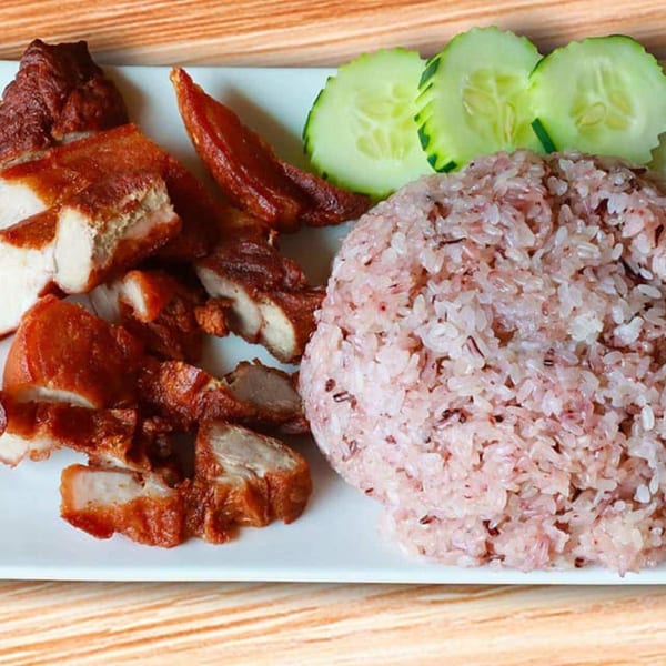 Som Jai Thai Cuisine's crispy pork belly with red rice and cucumber slices on a white plate.