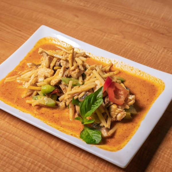 Som Jai Thai Cuisine's red curry with chicken, bamboo shoots, and basil on a white rectangular plate.
